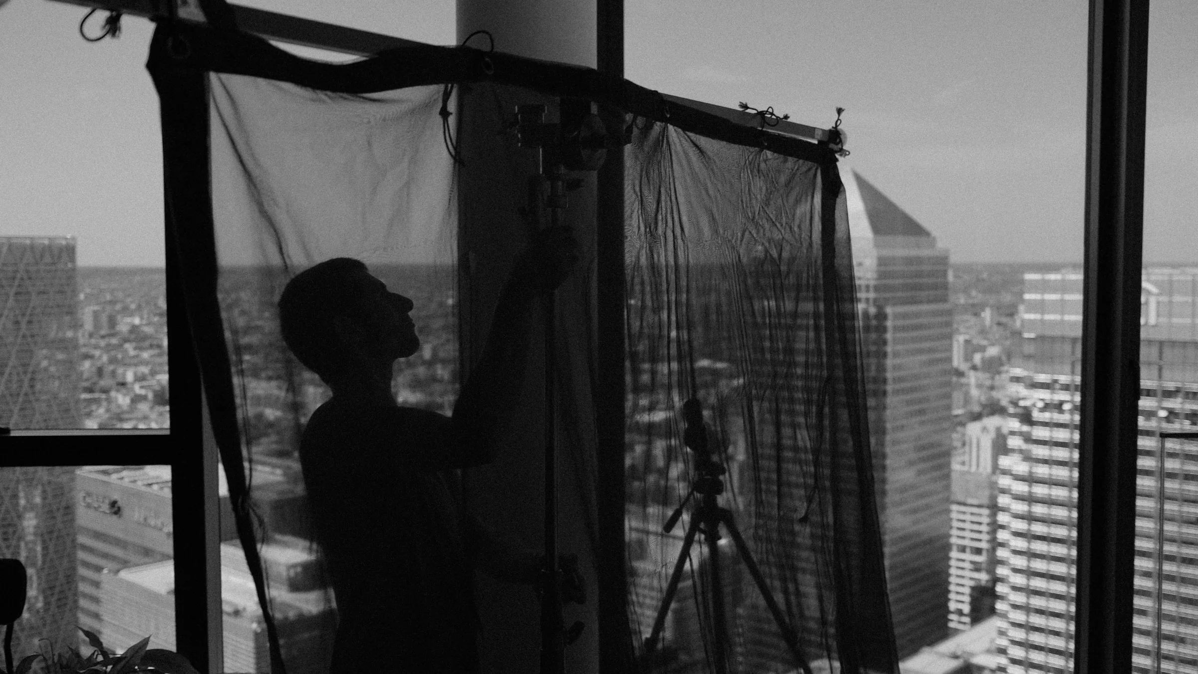 Crew member adjusting a diffusion frame beside a city window